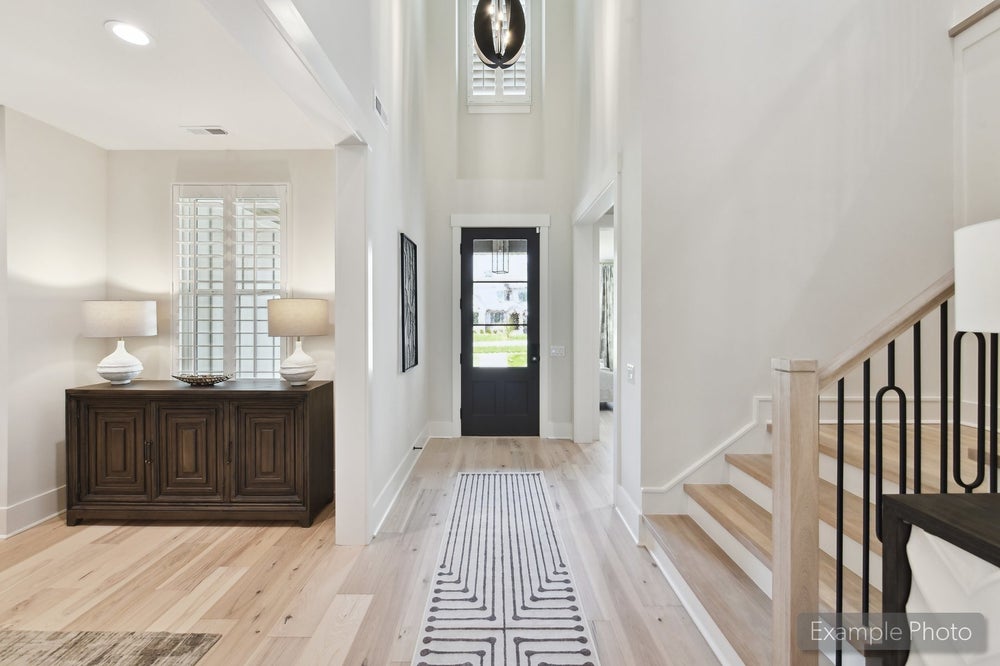 Bright foyer with two-story ceiling, black front door, hardwood floors, and staircase with iron balusters