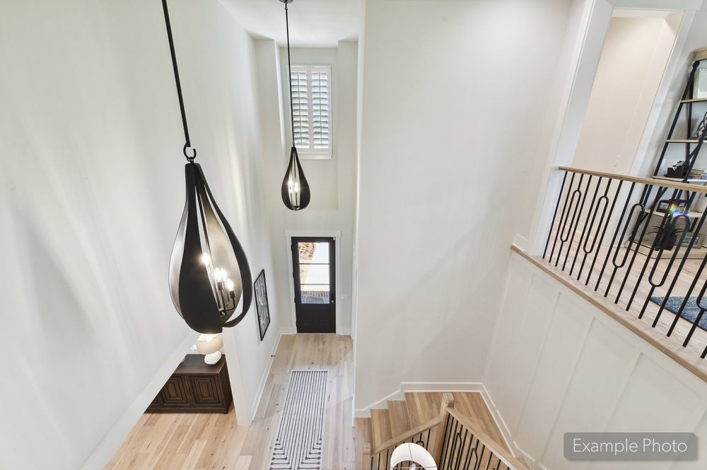 Two-story foyer with two black teardrop pendant lights, wood staircase with iron balusters, and light hardwood floors