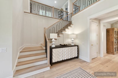 Two-story foyer with wood and iron staircase, light hardwood floors, and decorative console table with lamps