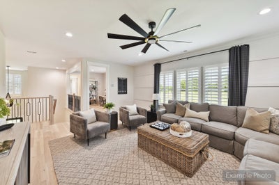 Bright living room with gray sectional sofa, wicker coffee table, and large ceiling fan near staircase landing