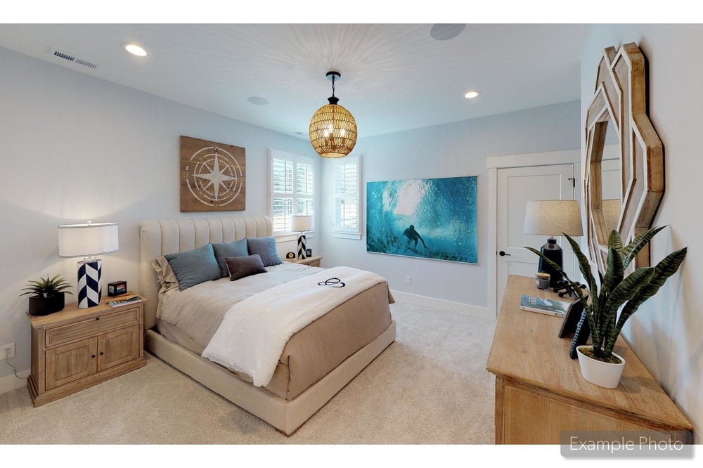 Bedroom with upholstered bed, rattan pendant light, wood nightstands, and coastal-themed wall art on carpet flooring