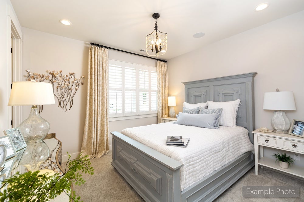 Bedroom with gray wood bed frame, pendant light, plantation shutters, and neutral carpet