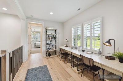 Upstairs loft study area with built-in desk, three chairs, open shelving, and plantation shutters on large windows