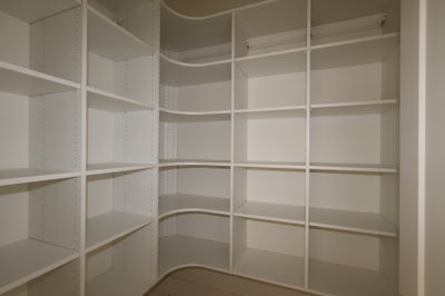 Empty walk-in closet with white built-in shelving units and a hanging rod along three walls