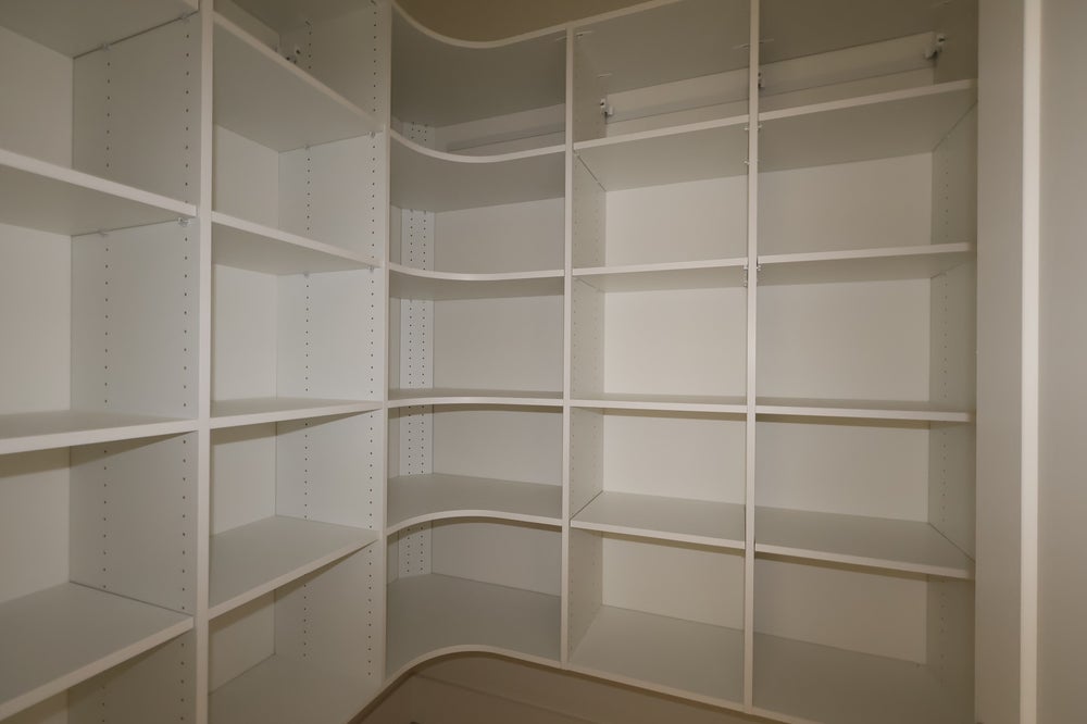 Empty walk-in closet with white built-in shelving units and a hanging rod along three walls