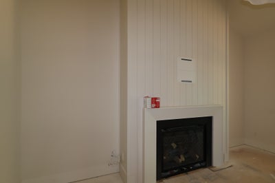 White fireplace with shaker-style wood panel surround and black firebox insert in an empty room under construction