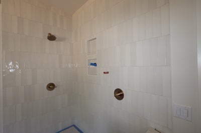 Tiled shower with white vertical subway tiles, built-in niche, rain showerhead, and brushed nickel fixtures under construction