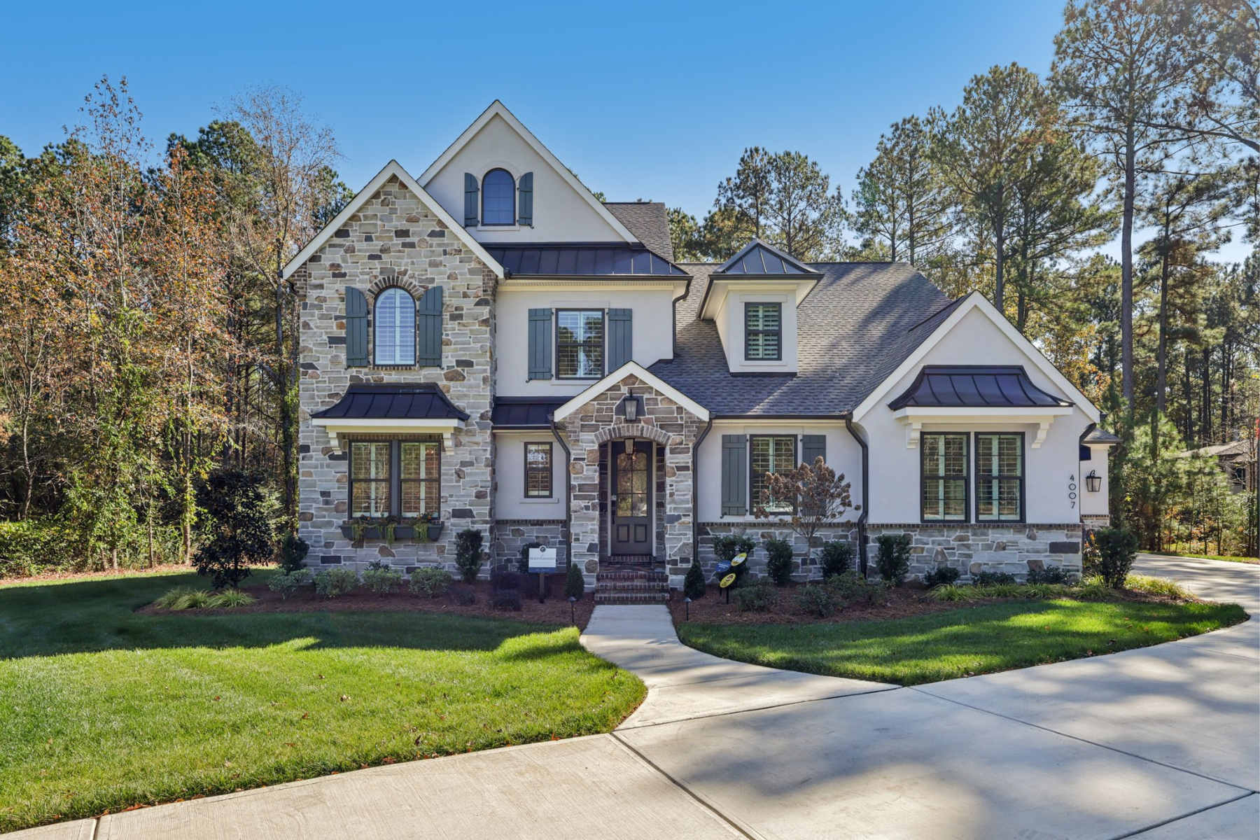 Two-story home with stone and white stucco exterior, dark shutters, arched entry, and manicured front lawn