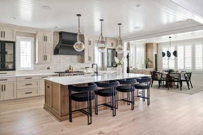 Open kitchen with large island, black barstools, pendant lights, and light wood floors opening to dining area