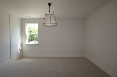 Empty bedroom with neutral carpet, white walls, single window, and pendant light fixture