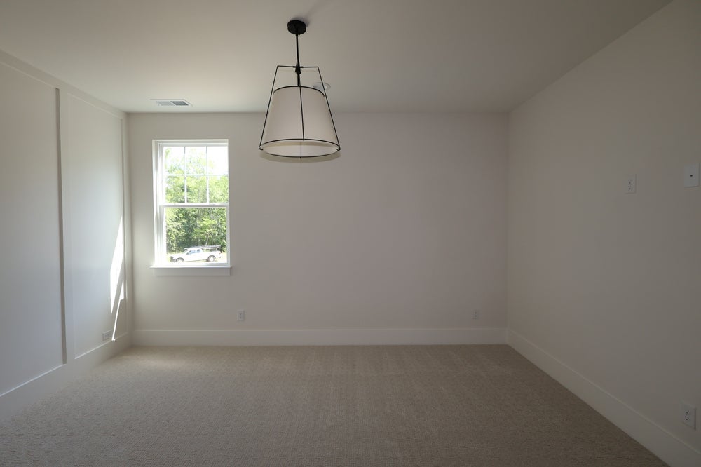 Empty bedroom with neutral carpet, white walls, single window, and pendant light fixture