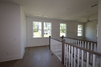 Second-floor hallway with wood railing, hardwood floors, shiplap accent wall, and multiple windows