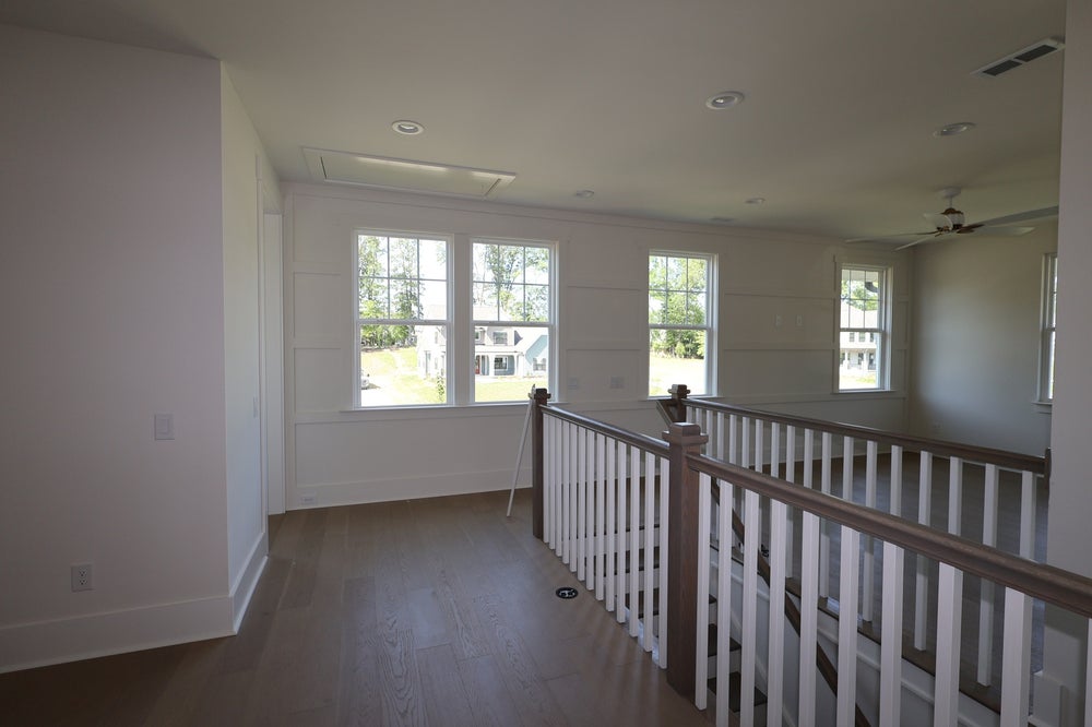 Second-floor hallway with wood railing, hardwood floors, shiplap accent wall, and multiple windows