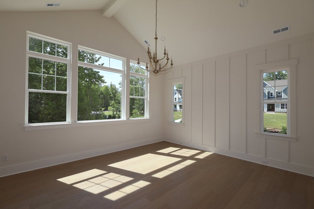Empty room with vaulted ceiling, hardwood floors, board and batten wall, and large windows with a brass chandelier