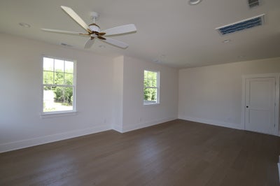 Empty bedroom with hardwood floors, ceiling fan, two windows, and white walls