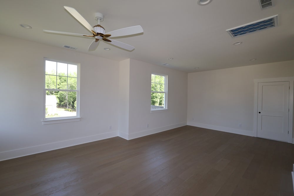 Empty bedroom with hardwood floors, ceiling fan, two windows, and white walls