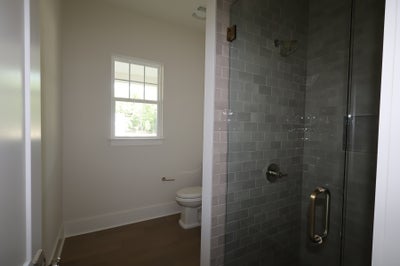 Bathroom with glass-enclosed shower with gray subway tiles, toilet, and small window