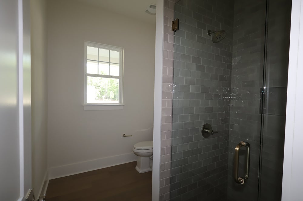 Bathroom with glass-enclosed shower with gray subway tiles, toilet, and small window