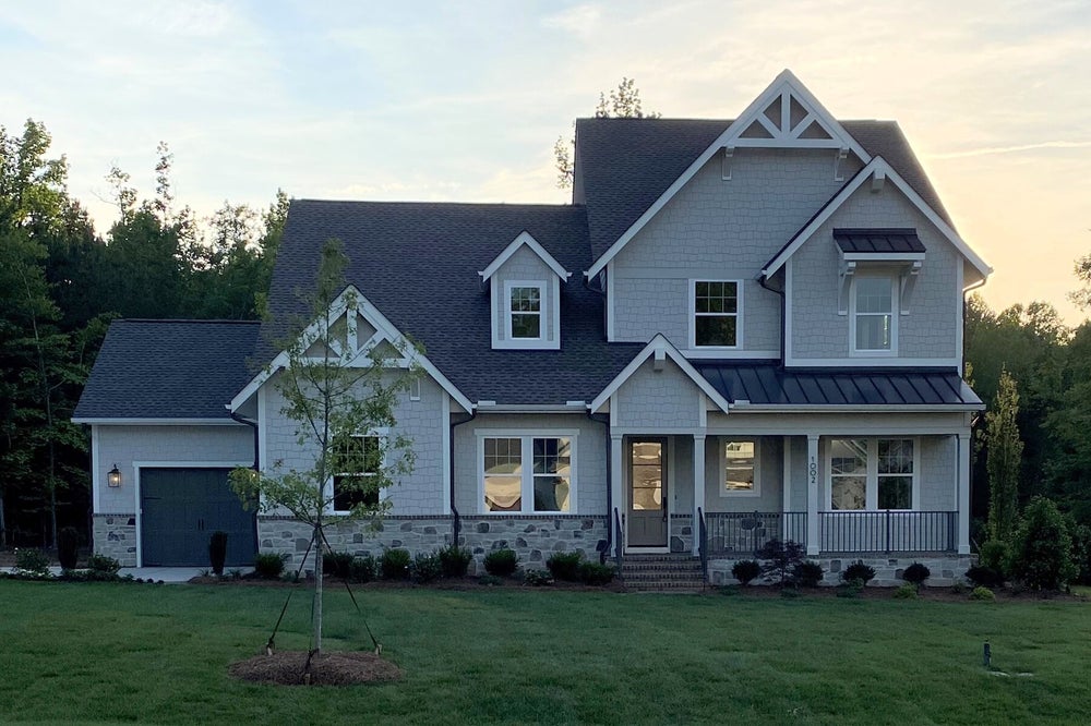 Two-story craftsman home with gray siding, stone foundation, covered porch, and attached garage surrounded by green lawn