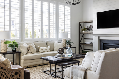 Living room with beige sofa, shiplap fireplace wall, wall-mounted TV, and plantation shutters on large windows