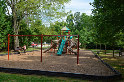 Neighborhood playground with swing set, multiple slides, and wood chip ground cover surrounded by trees