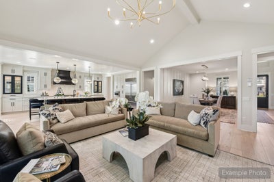 Open-concept living room with vaulted ceiling, gold chandelier, and kitchen visible in background