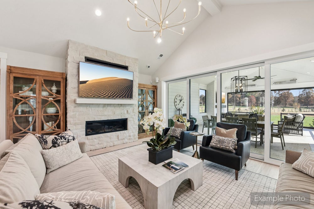 Living room with vaulted ceiling, stone fireplace, wall-mounted TV, and sliding glass doors to covered patio
