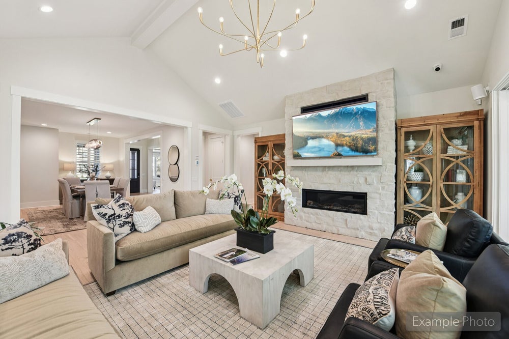 Living room with vaulted ceiling, stone fireplace, wall-mounted TV, and gold chandelier