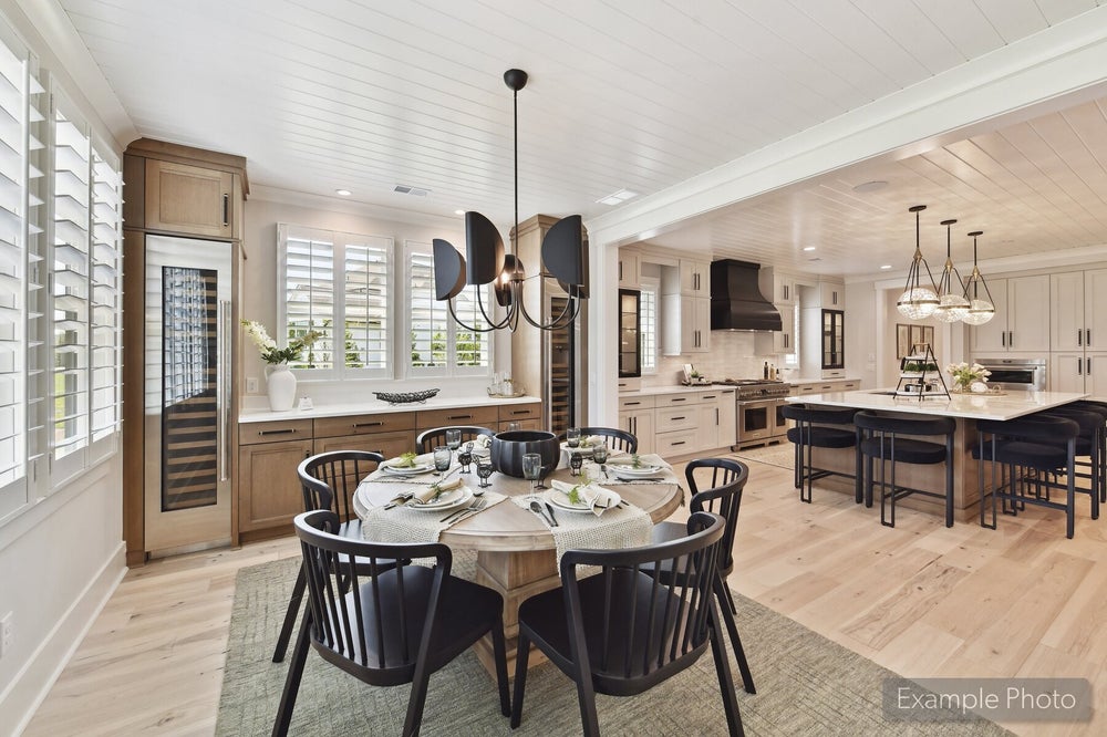 Open-concept dining area with round table and black chairs flowing into white kitchen with large island and hardwood floors