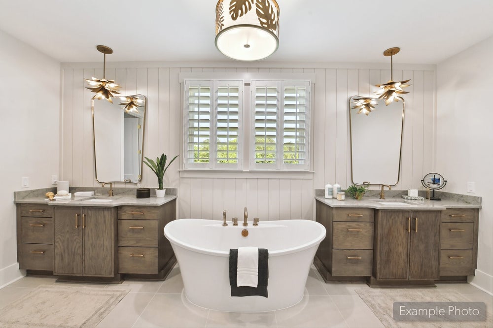 Master bathroom with freestanding soaking tub, dual wood vanities, gold fixtures, and shiplap accent wall