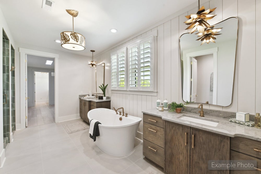 Master bathroom with freestanding soaking tub, wood vanities, marble countertops, and decorative gold pendant lights