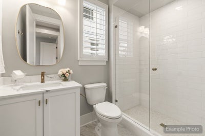 Bathroom with white vanity, marble countertop, glass walk-in shower with subway tile, and oval gold-framed mirror
