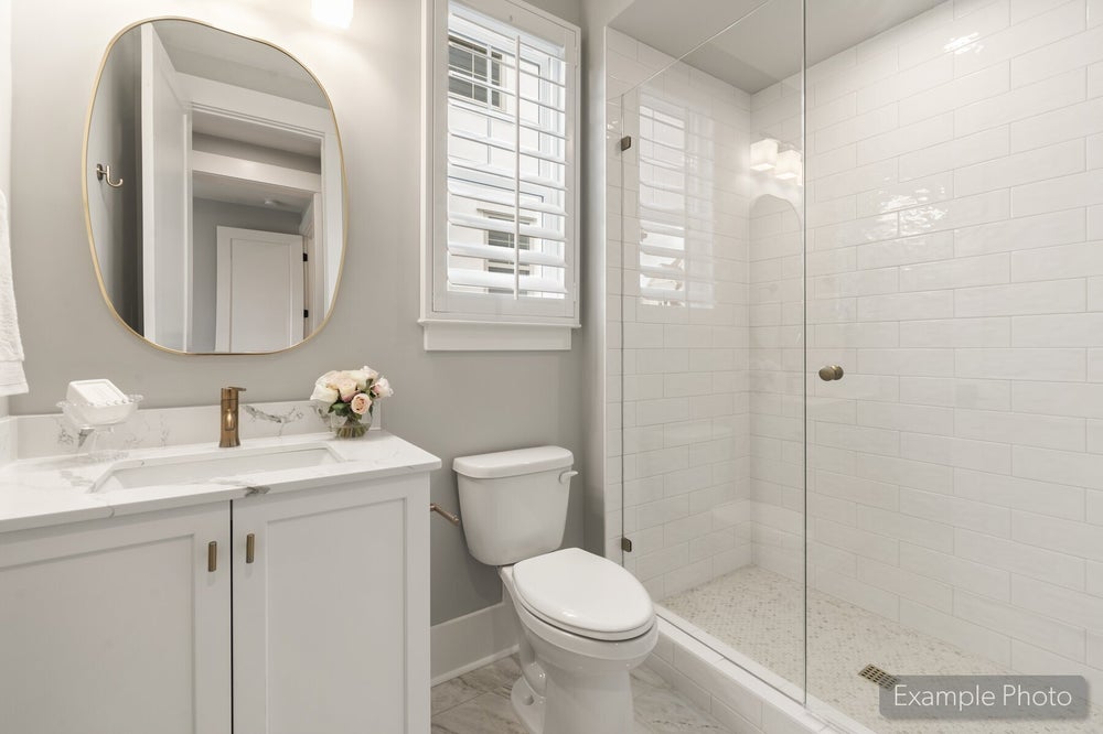 Bathroom with white vanity, marble countertop, glass walk-in shower with subway tile, and oval gold-framed mirror