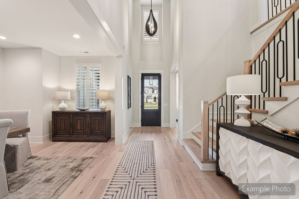 Bright two-story foyer with hardwood floors, staircase with iron balusters, and black front door