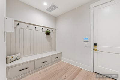 Mudroom with built-in bench, storage drawers, coat hooks, and light hardwood floors near entry door