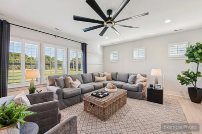 Living room with gray sectional sofa, wicker coffee table, large ceiling fan, and tall windows with backyard views