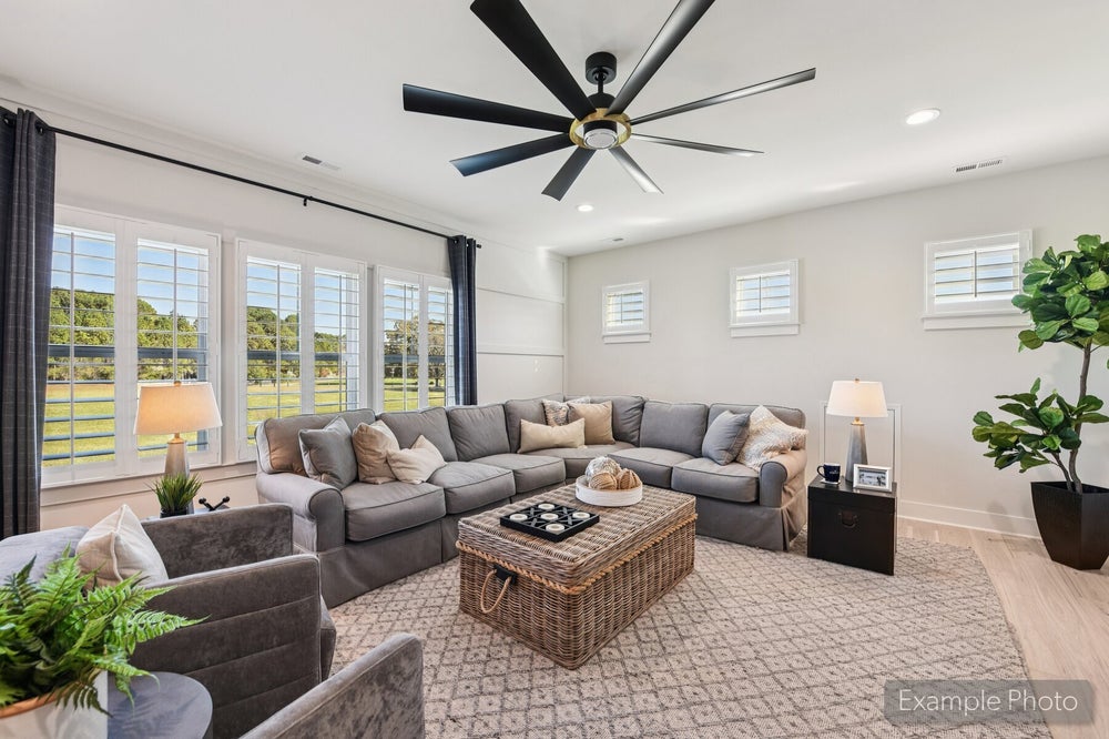 Living room with gray sectional sofa, wicker coffee table, large ceiling fan, and tall windows with backyard views