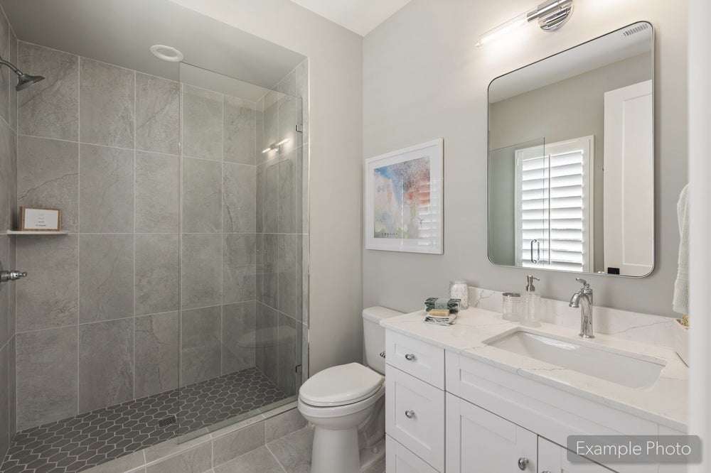 Bathroom with glass walk-in shower, gray tile walls, white vanity, and quartz countertop