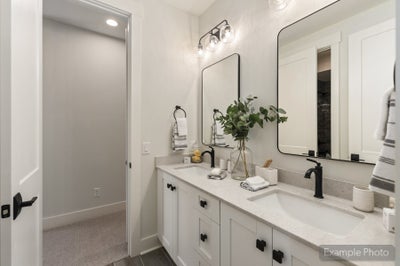 Bathroom with double vanity, white cabinets, stone countertops, and black fixtures with two mirrors above