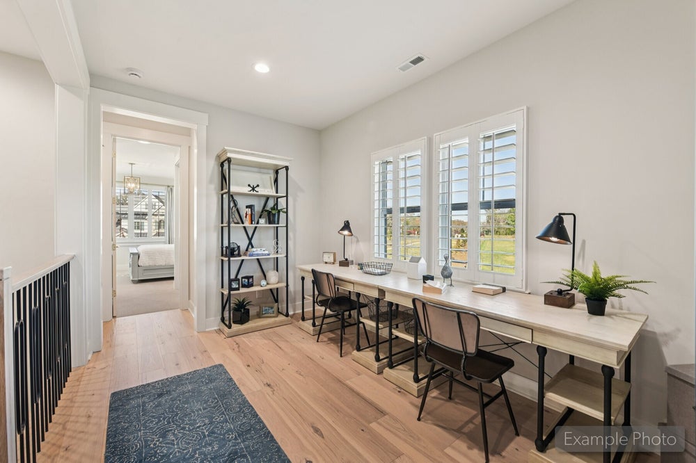 Loft study area with long desk, three chairs, open shelving, and plantation shuttered windows over hardwood floors