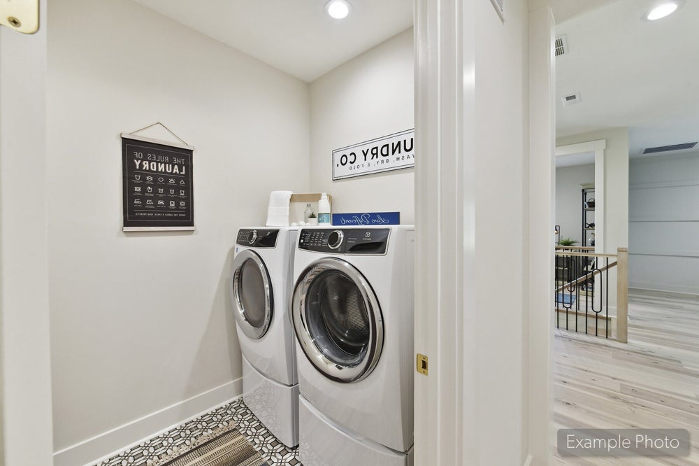 Laundry room with front-load washer and dryer on pedestals and decorative tile floor