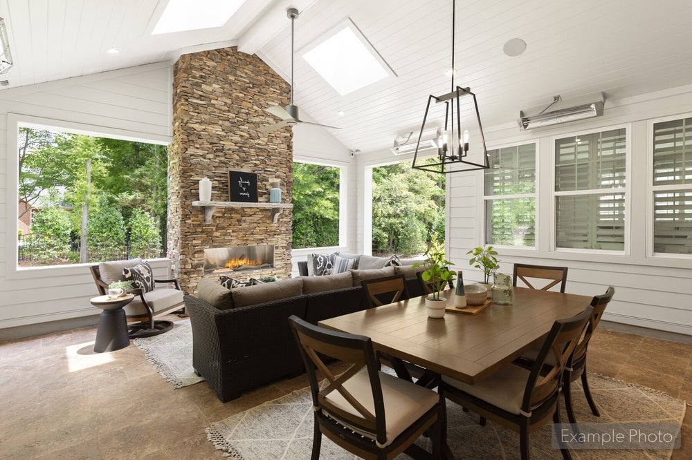 Screened porch with tall stone fireplace, vaulted ceiling, dining table, and sectional sofa