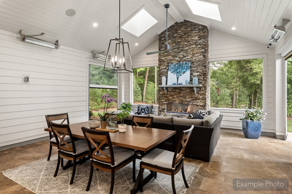 Sunroom with vaulted ceiling, stone fireplace, dining table, and seating area with large windows