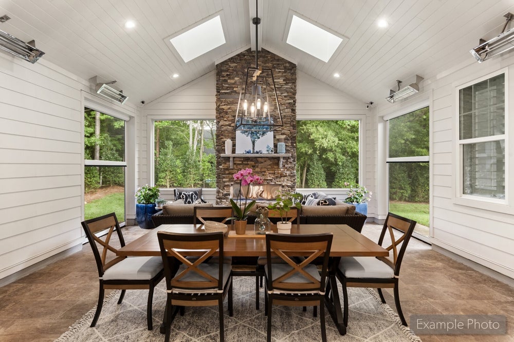 Sunroom dining area with vaulted shiplap ceiling, skylights, stone fireplace, and wood dining table for six