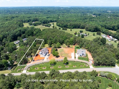 Aerial view of Lot 1 with a home under construction, surrounded by trees and neighboring houses in a wooded subdivision.