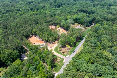 Aerial view of a wooded residential development with cleared lots under construction and a paved road entrance.