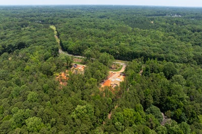 Aerial view of new home construction sites with cleared red clay lots surrounded by dense green forest