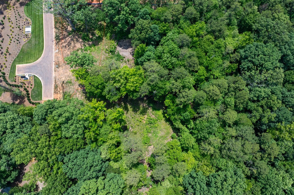 Aerial view of a wooded residential lot with a paved cul-de-sac street and manicured lawn nearby