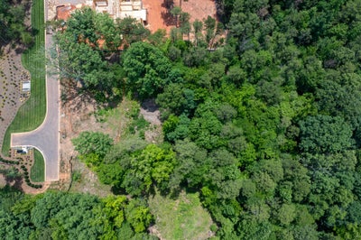 Aerial view of wooded residential lot with nearby home under construction and curved street access