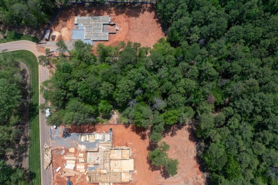 Aerial view of two homes under construction on wooded lots with red clay soil and framed foundations visible.